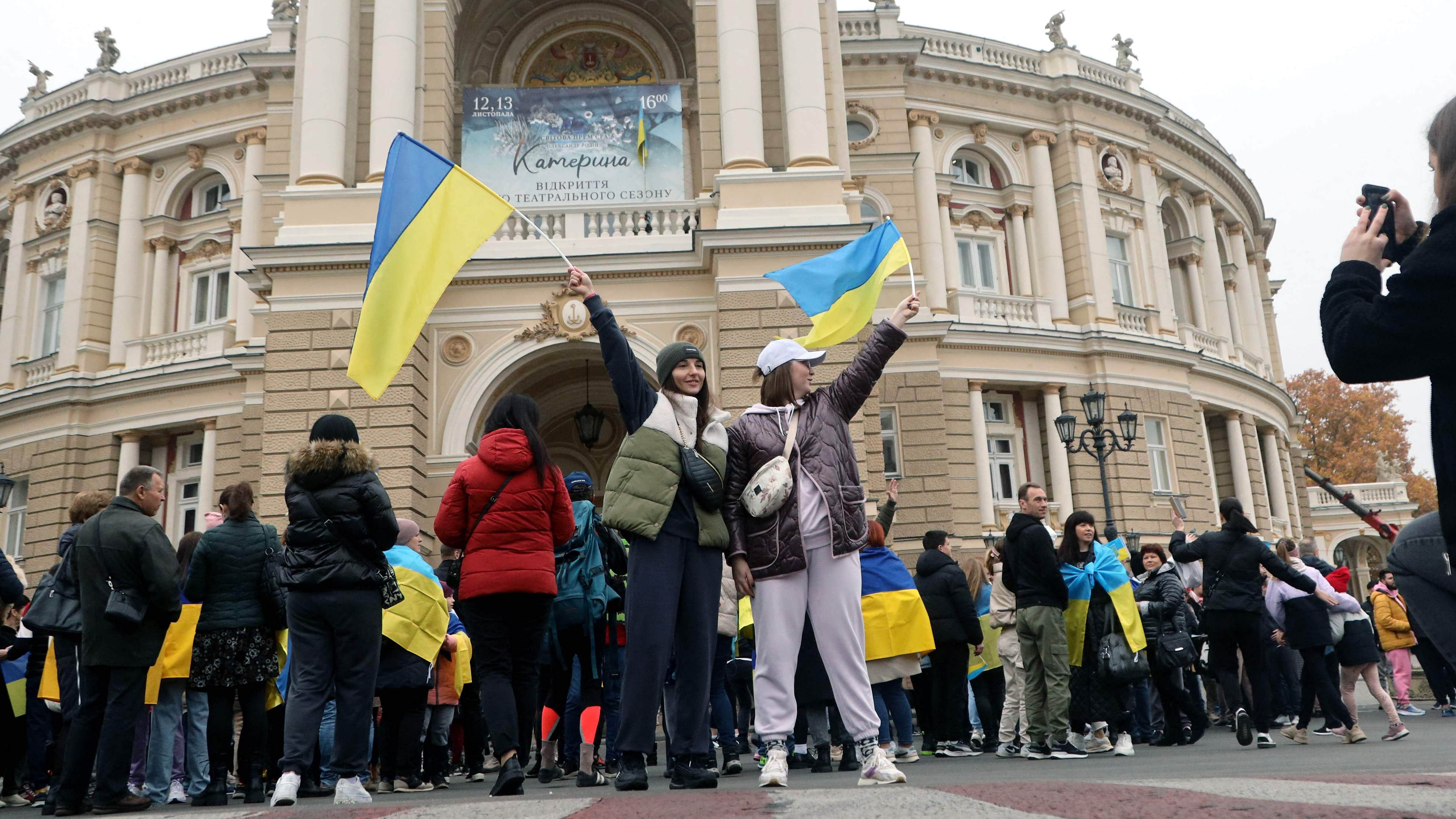 Residents of Kherson temporarily living in Odessa, holding Ukrainian flags, celebrate the liberation of their native town in front of The Odessa National Academic Opera and Ballet. Credit: AFP Photo