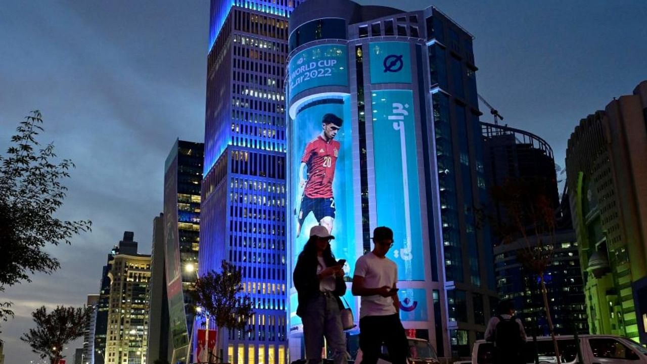 People walk in front of an image of Spain's midfielder Pedri decorating a building in Doha on November 17, 2022, ahead of the Qatar 2022 World Cup football tournament. Credit: AFP Photo