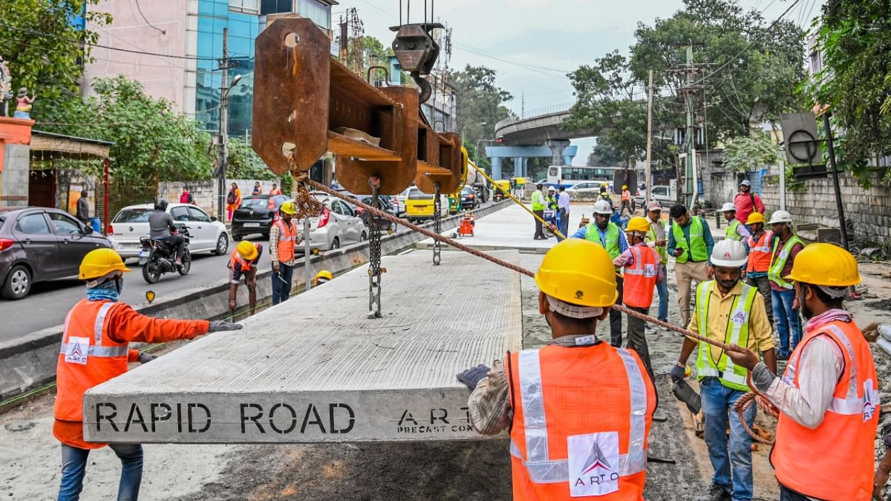 Workers white-top Old Madras Road on Tuesday. Under the new project, the civic body aims to fabricate the concrete slabs in the factory and embed them on the road. Credit: DH Photo