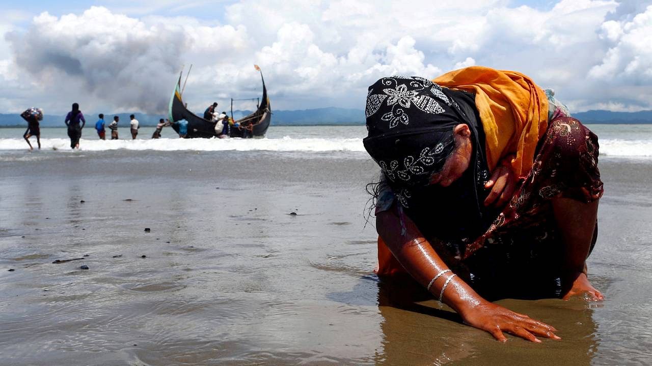 An exhausted Rohingya refugee woman touches the shore after crossing the Bangladesh-Myanmar border by boat through the Bay of Bengal. Credit: Reuters File Photo