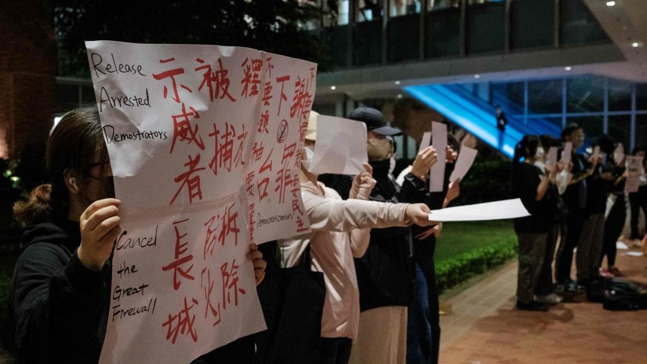 Protesters hold up a sign (L) and sheets of blank paper at the University of Hong Kong campus in solidarity with demonstrations in mainland China against strict Covid restrictions and demanding for greater freedoms, in Hong Kong. Credit: AFP Photo