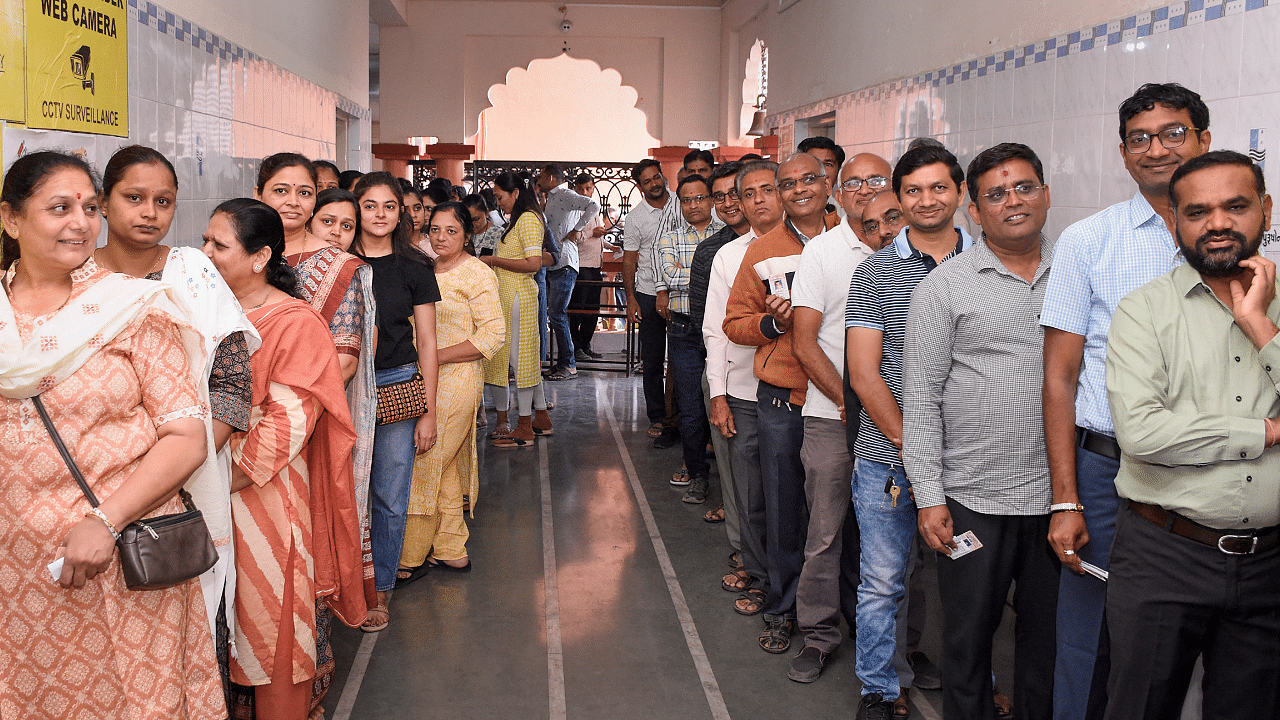 People wait in queues at a polling station to cast their votes during the first phase of Gujarat Assembly elections, in Surat. Credit: PTI Photo