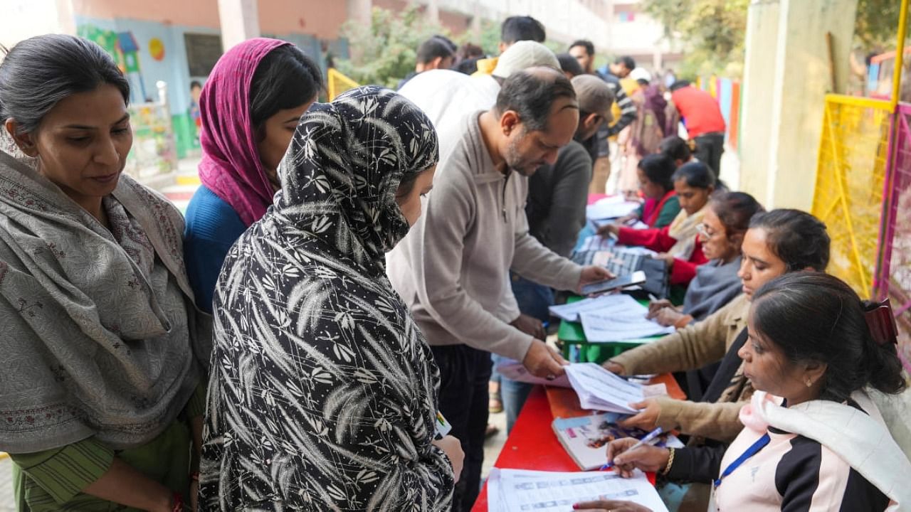 Polling agents look for the names of the people in a list as they come to cast their votes for the MCD elections, Delhi. Credit: PTI Photo