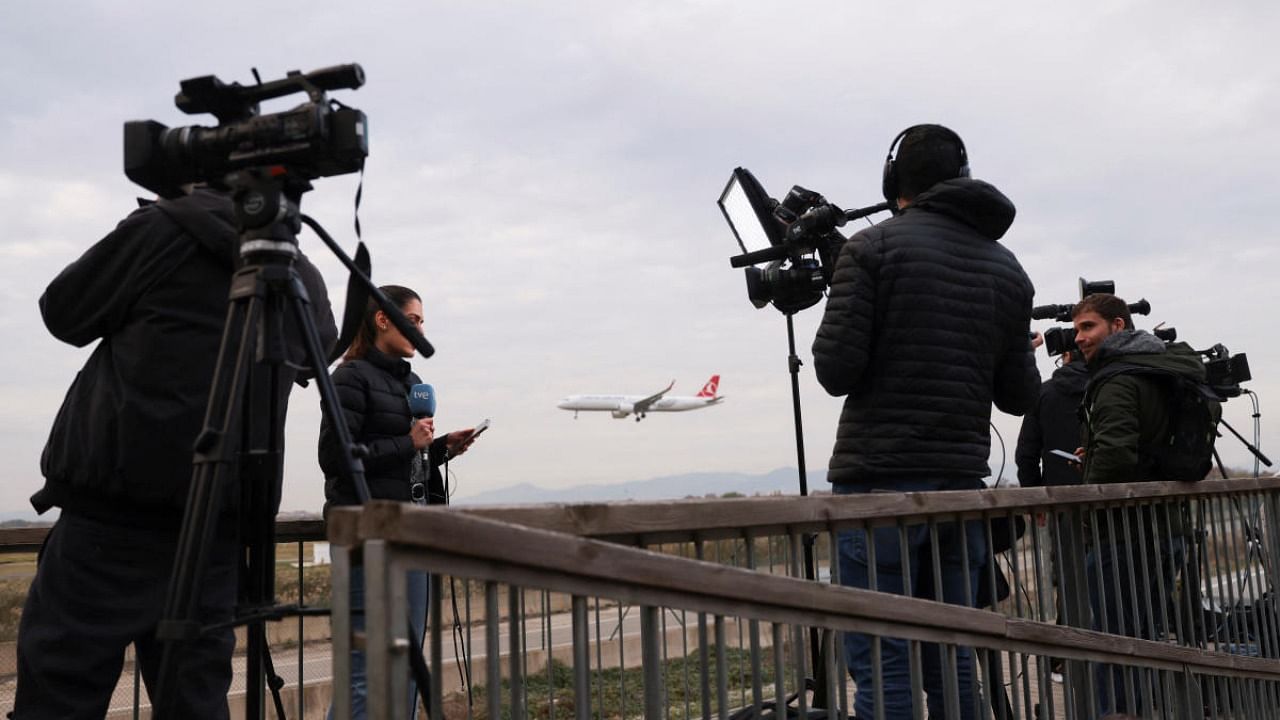 A plane flies in the background as journalists work, after a commercial airplane flying from Morocco to Turkey made an emergency landing in Barcelona's El Prat airport. Credit: Reuters photo
