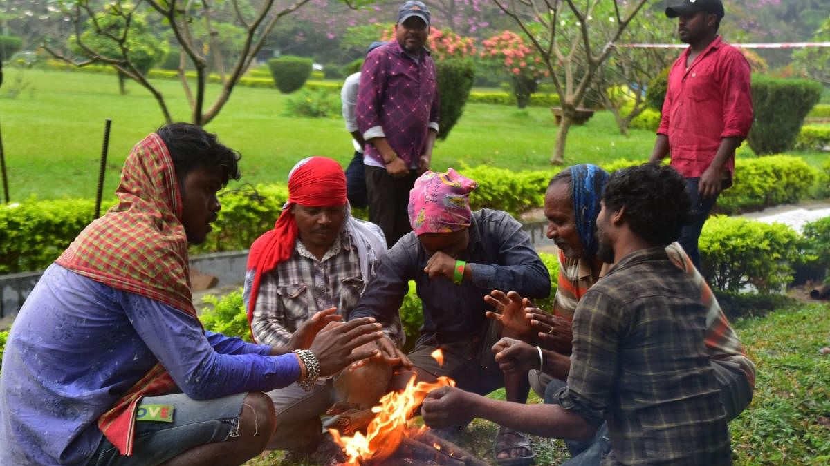 Workers warm up by lighting a fire in Cubbon Park as cold weather and drizzle marked Bengaluru on Friday. Credit:  DH Photo/Kishor Kumar Bolar