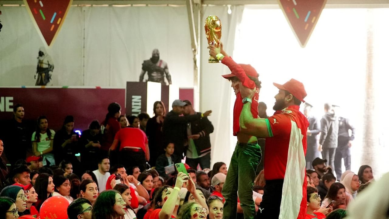  Morocco fan holds a replica World Cup trophy aloft while being lifted up by another fan. Credit: Reuters Photo