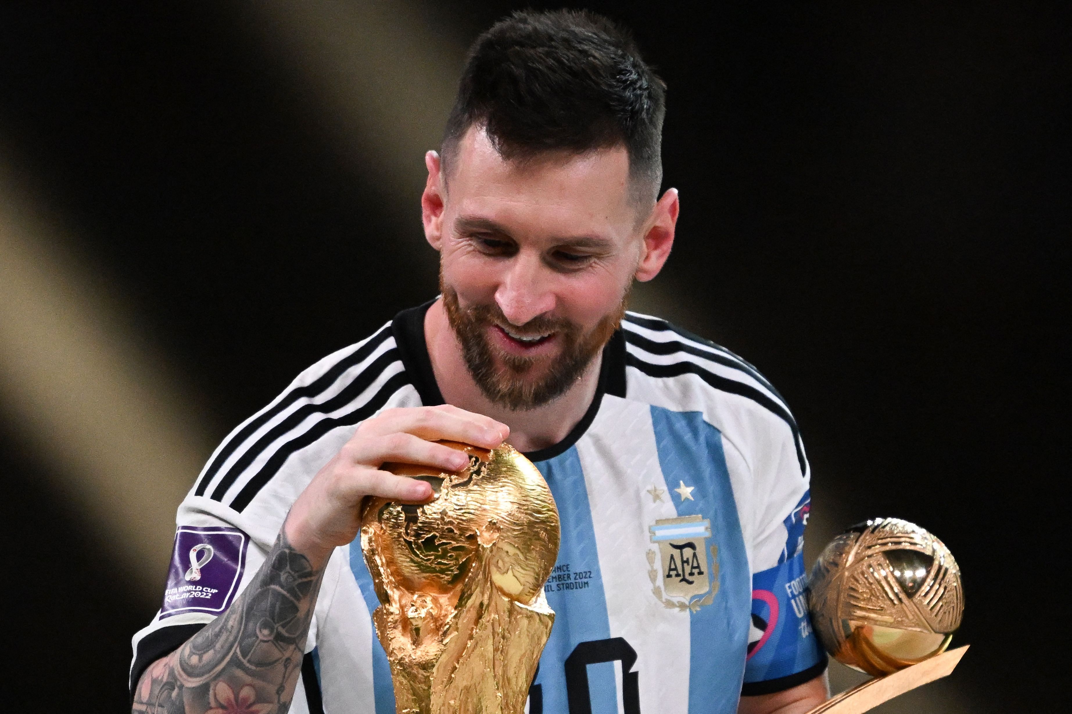 Lionel Messi smiles as he touches the FIFA World Cup Trophy during the trophy ceremony after Argentina won the Qatar 2022 World Cup final. Credit: AFP Photo