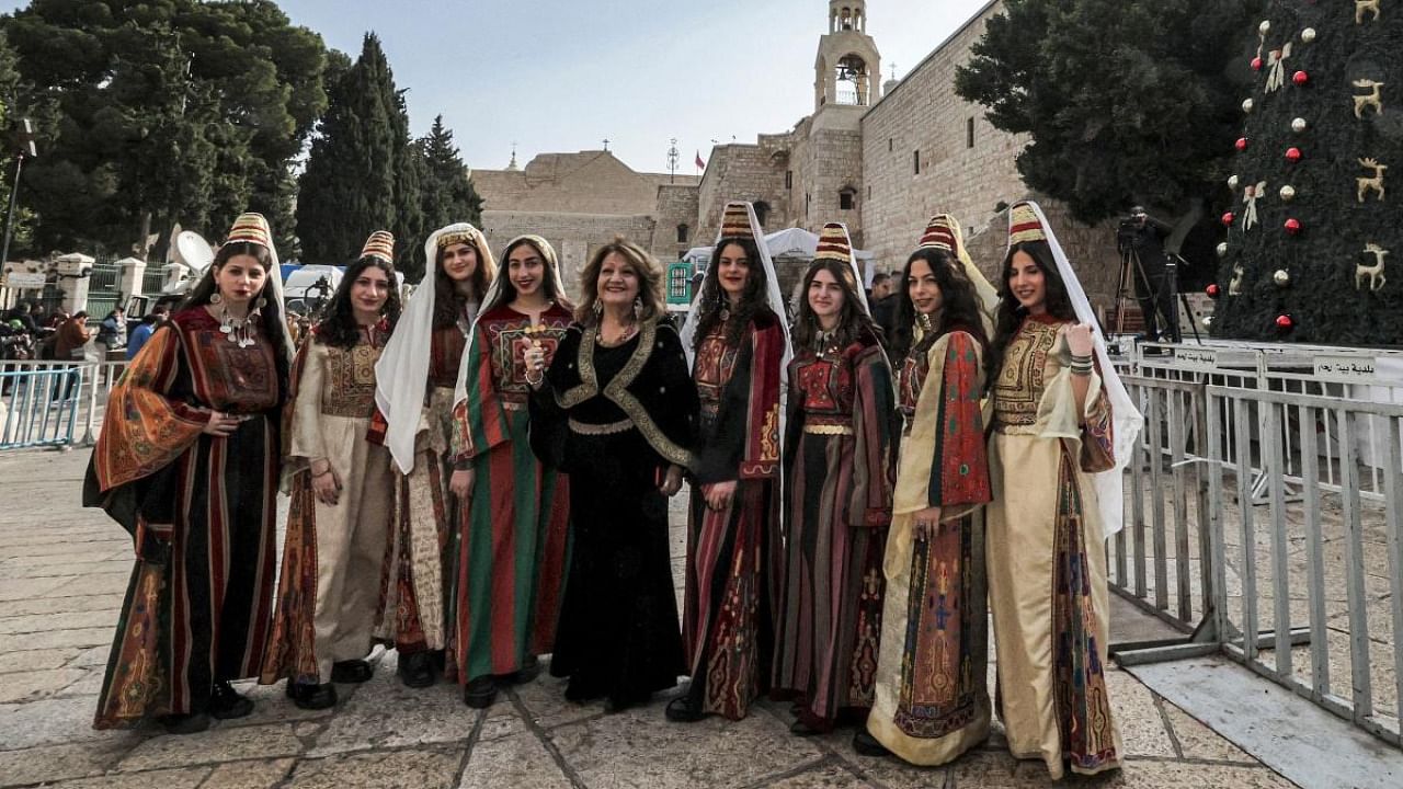 Women dressed in traditional clothing pose for a picture by the Christmas tree at the Manger Square outside the Church of the Nativity in the biblical city of Bethlehem in the occupied West Bank. Credit: AFP Photo