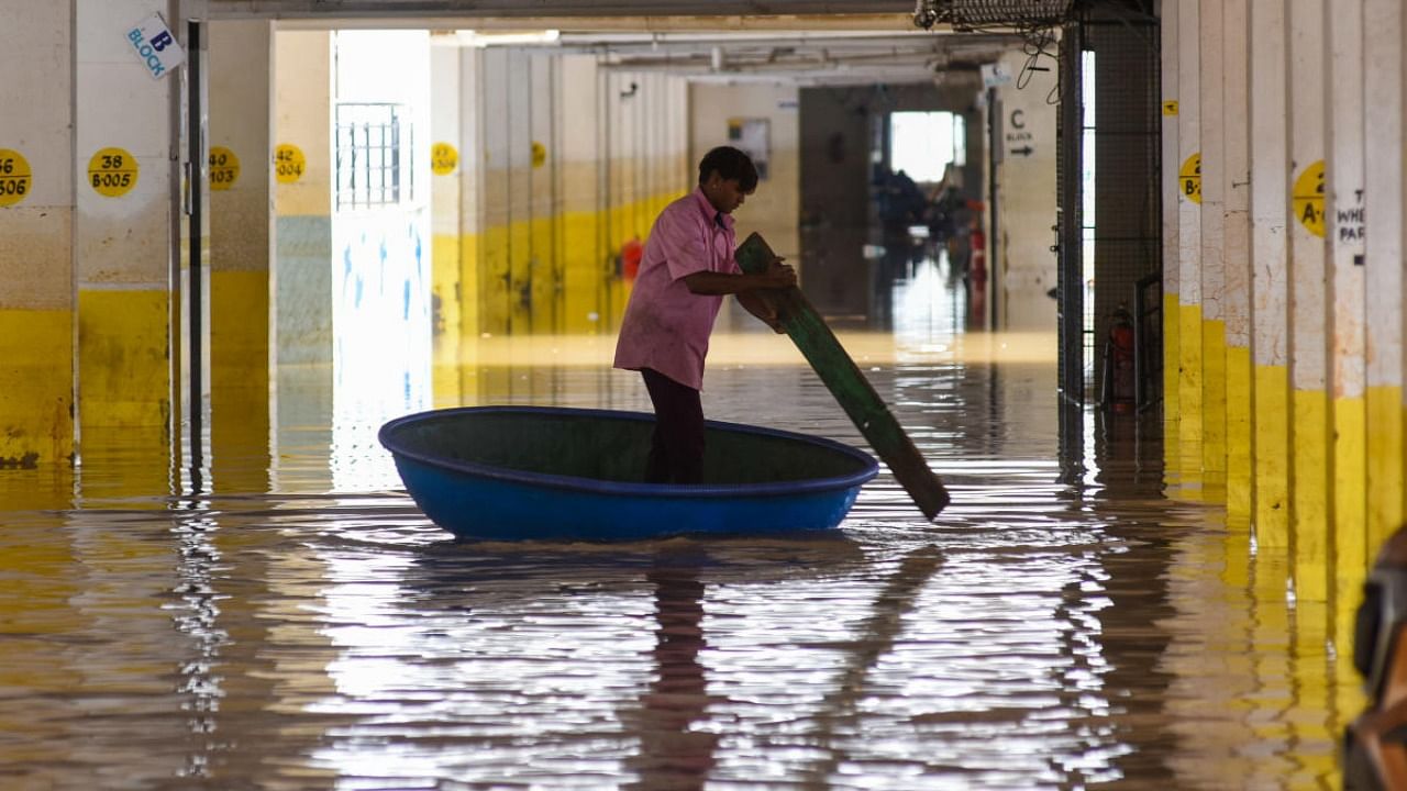 Unprecedented rains left Bengaluru's infrastructure in tatters in 2022 and BBMP was not up to the task in bringing solace to people. A man paddles a plastic coracle at the inundated basement of an apartment, following showers in Whitefield in September. Credit: DH File Photo