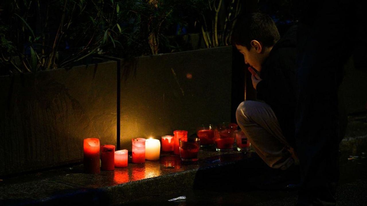 A child sits next to candles as a tribute to the victims of a shooting on December 23, 2022, in front of the "Centre democratique du Kurdistan" (Kurdistan democratic centre) in Paris on December 24, 2022. Credit: AFP Photo