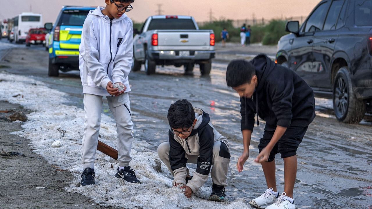 Children toss handfuls of hail particles picked up off the side of a road after a storm in the Umm al-Haiman district, about 55 kilometres south of Kuwait City, on December 27, 2022. Credit: AFP Photo