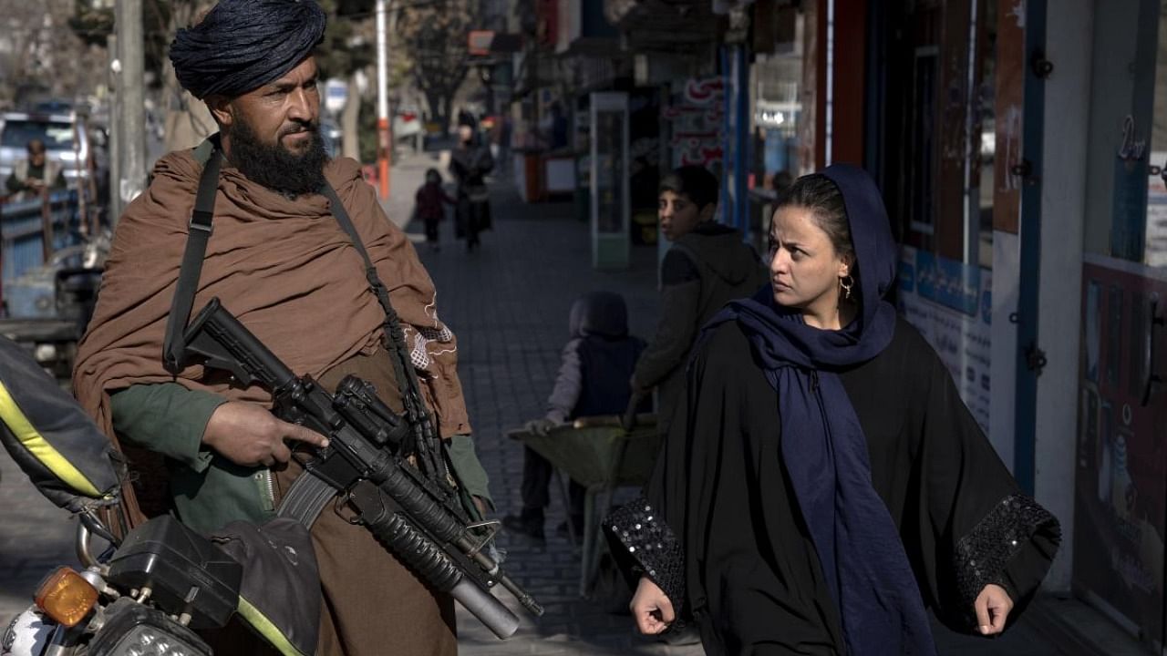A Taliban fighter stands guard as a woman walks past in Kabul, Afghanistan. Credit: AP/PTI Photo