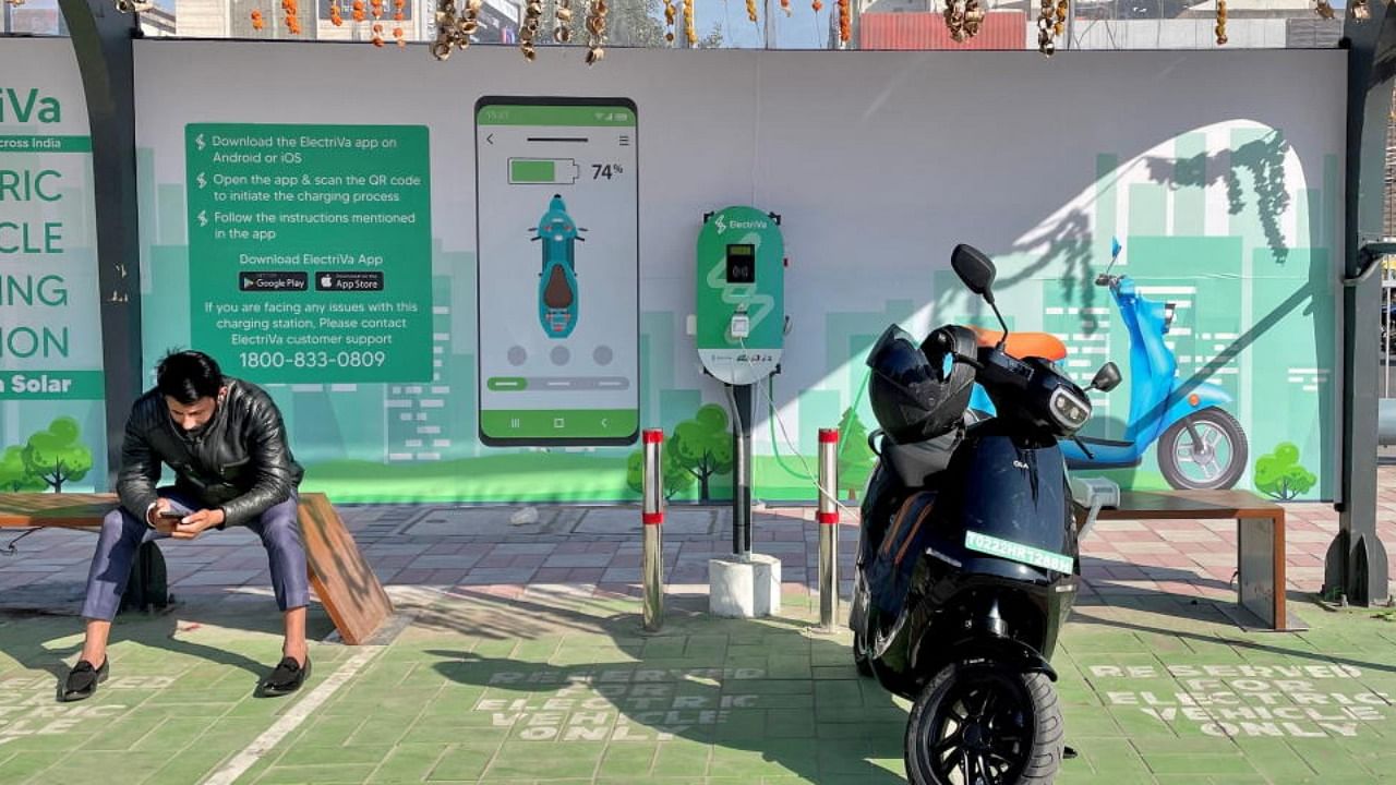 A man checks his mobile phone as he waits while recharging his Ola electric scooter, in New Delhi. Credit: Reuters Photo