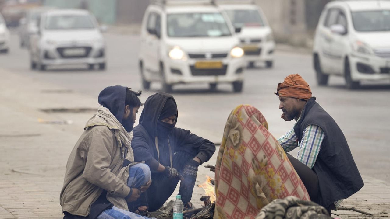 People sit around a bonfire to warm themselves on a cold winter morning, in New Delhi, Tuesday. Credit: PTI Photo