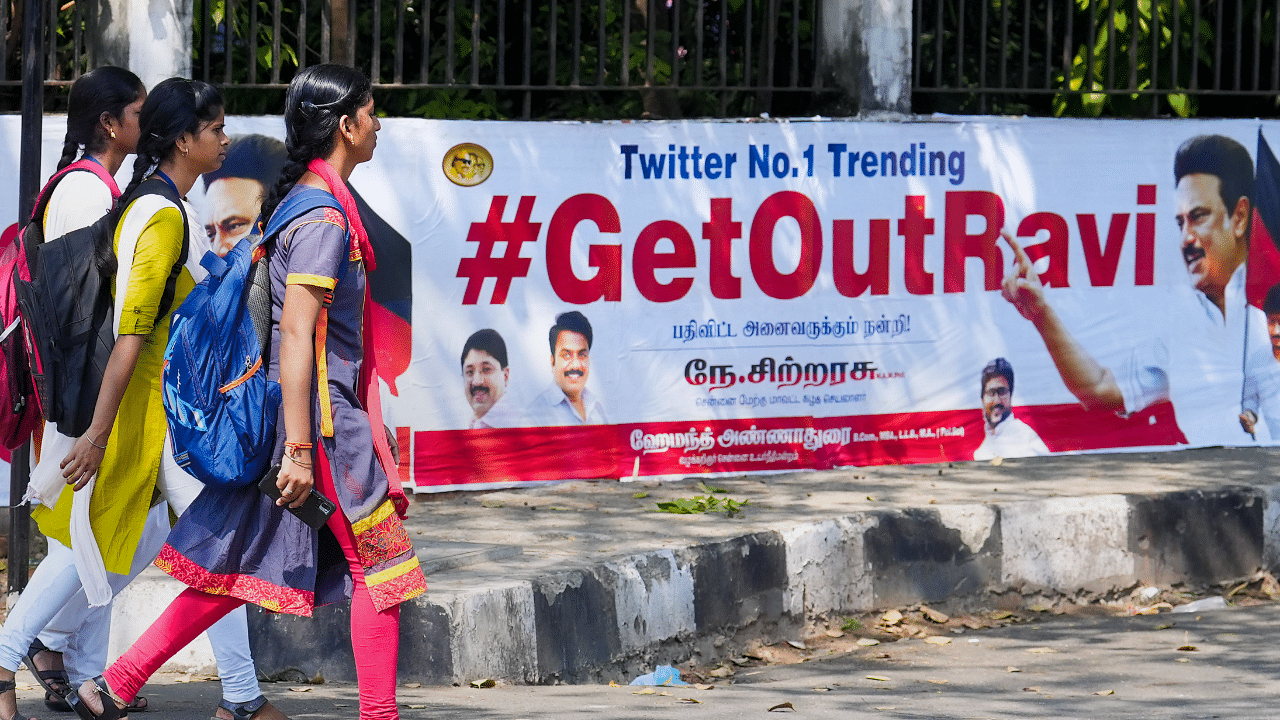 Young women walk past posters that read '#GetOutRavi' pasted on a wall, a day after Tamil Nadu Governor R.N. Ravi walked out of the State Assembly during Assembly Session, in Chennai. Credit: PTI Photo