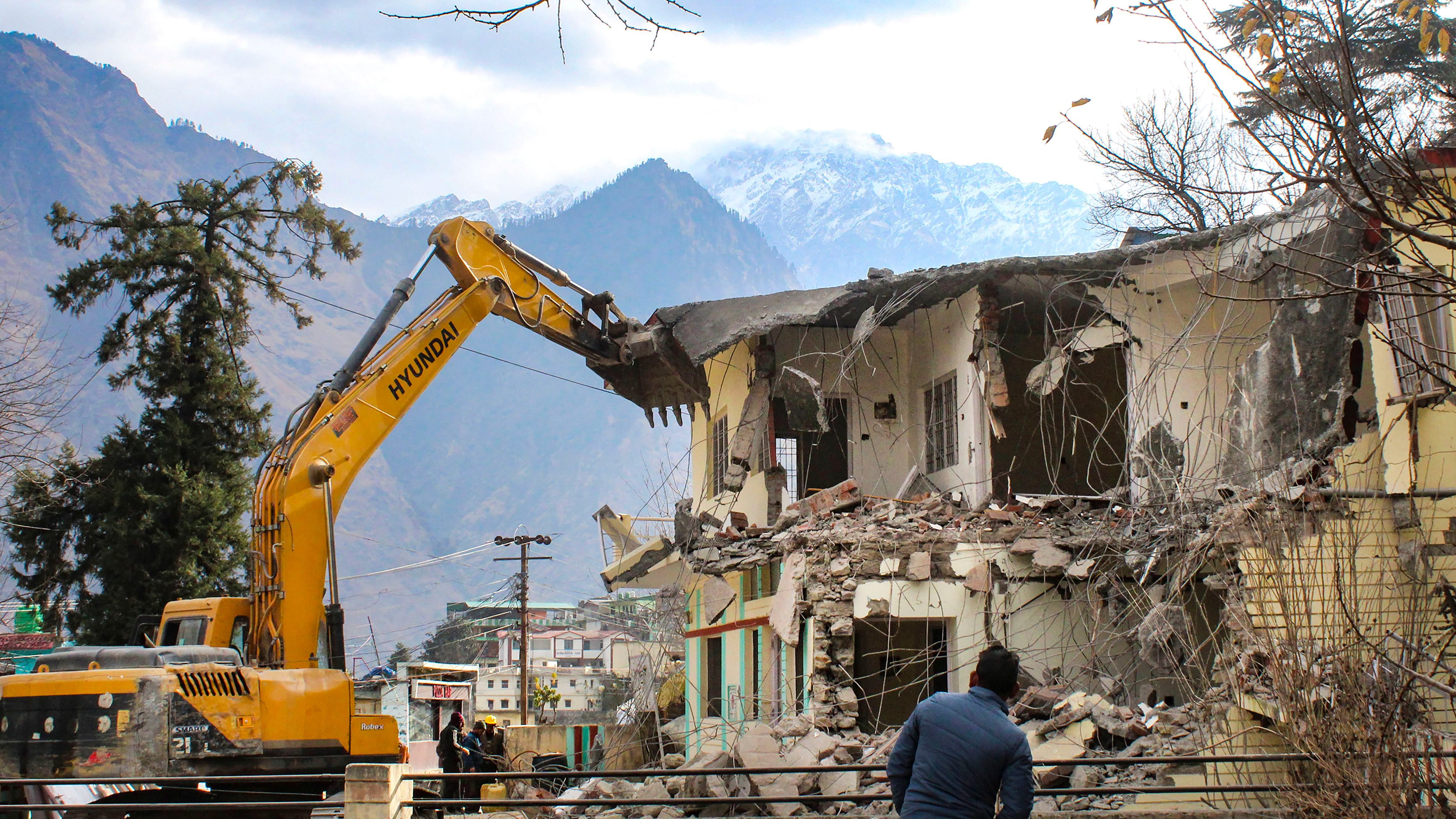 Workers use heavy machinery to demolish PWD guest house building which has been marked unsafe at a land subsidence affected area, in Joshimath. Credit: PTI File Photo