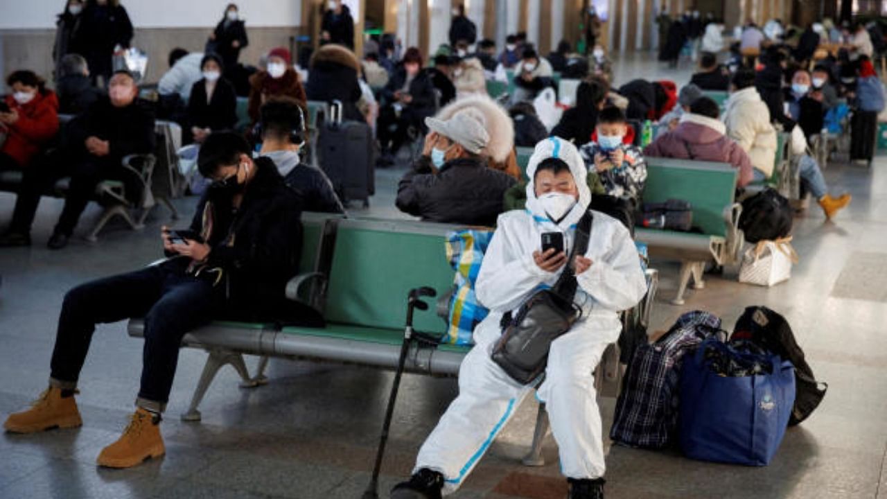 A person wearing a protective suit sits in Beijing Railway Station as passengers wait. Representative Image. Credit: Reuters File Photo
