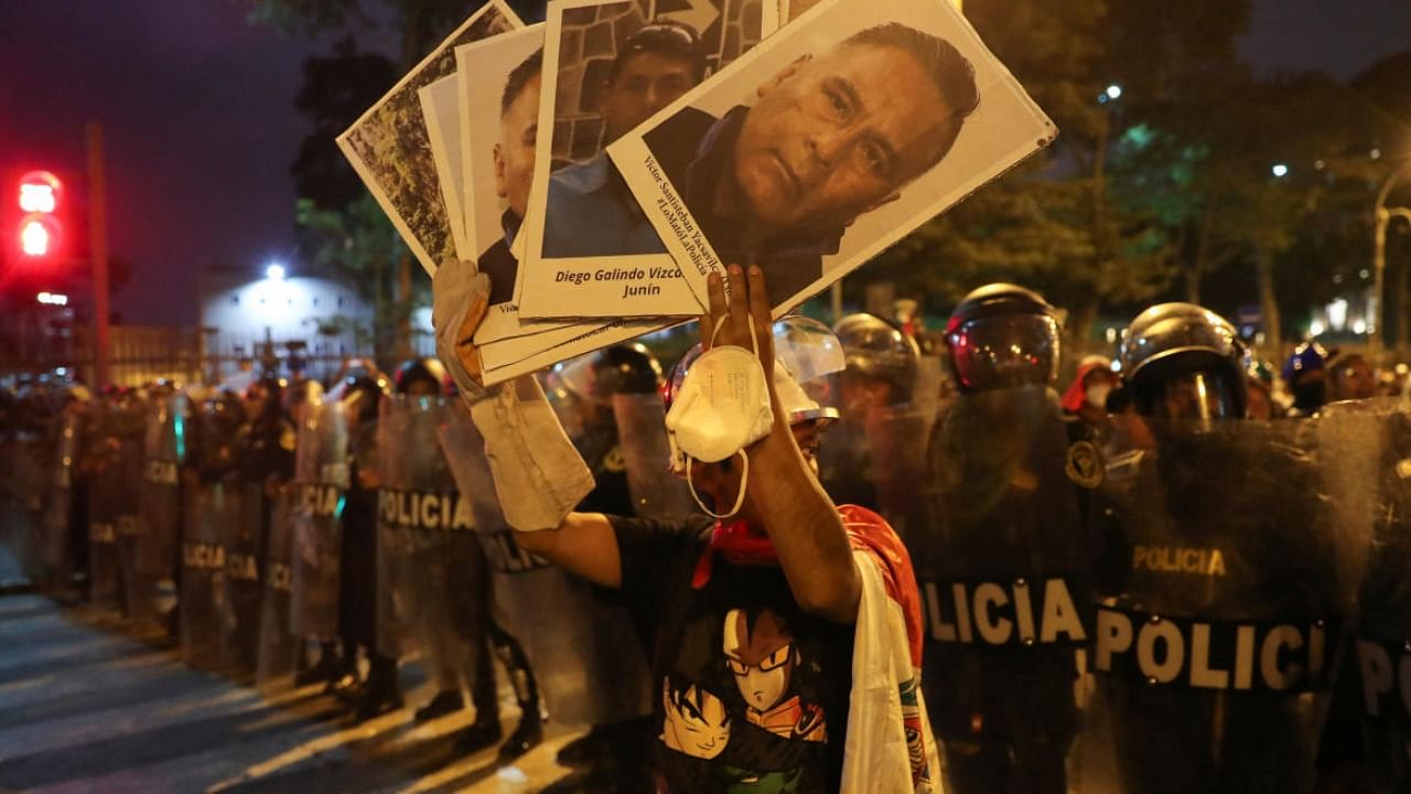 A demonstrator holds placards in front of riot police officers during a protest to demand Peru's President Dina Boluarte to step down, in Lima. Credit: Reuters