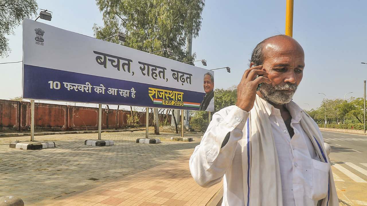 A man talks on mobile phone in the backdrop of a hoarding on upcoming Rajasthan Budget 2023-24 in Jaipur. Credit: PTI Photo