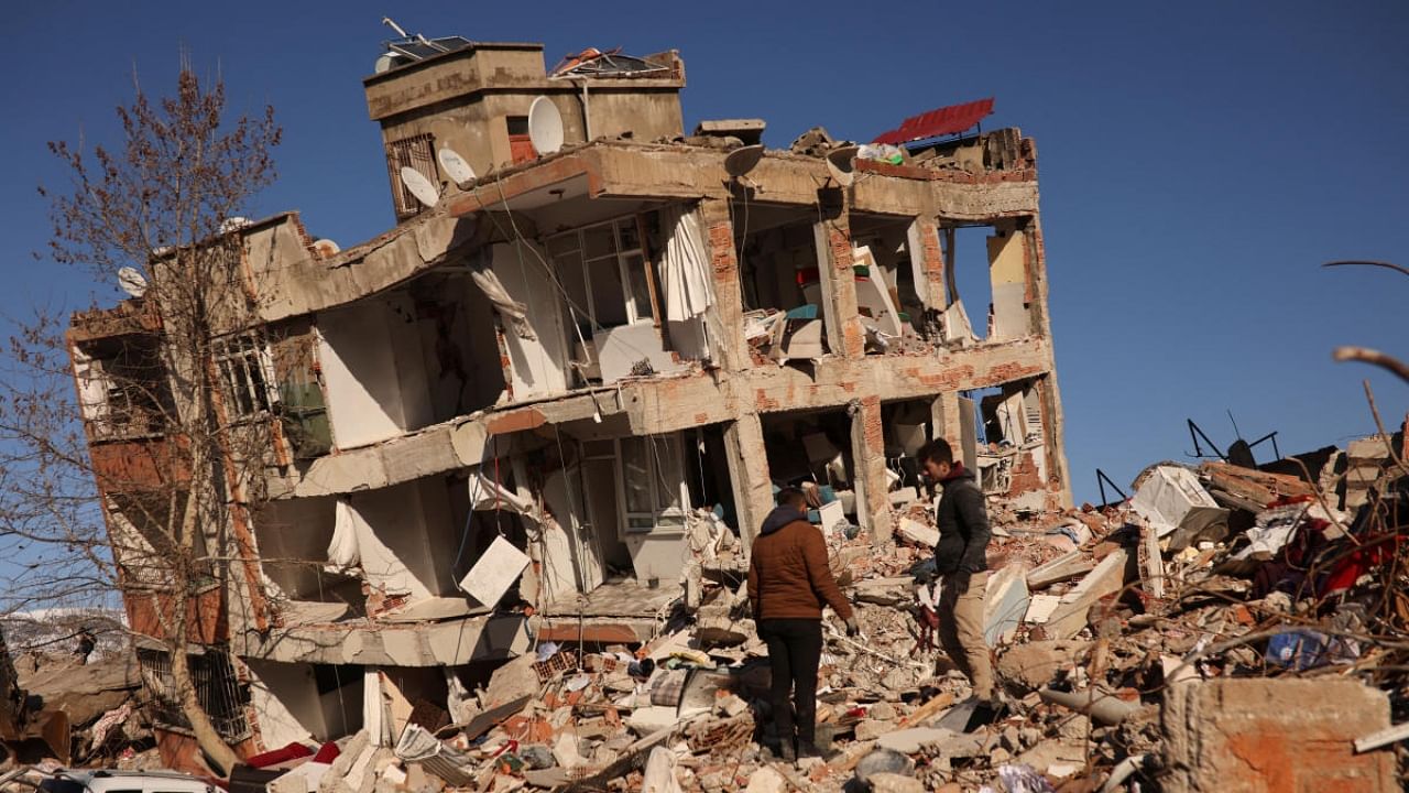 People stand next to a collapsed building, in the aftermath of a deadly earthquake in Kahramanmaras, Turkey. Credit: Reuters Photo