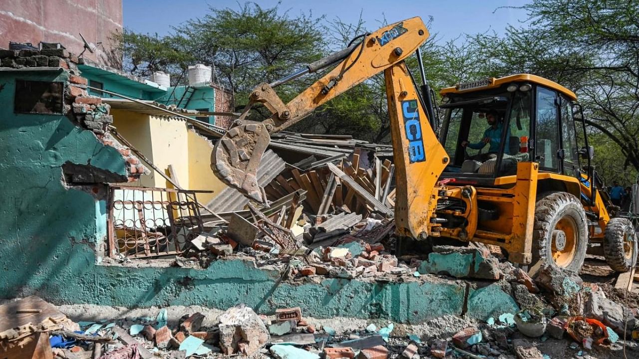 A backhoe loader demolishes a residential building during a demolishing drive of illegal constructions in Mehrauli area, in New Delhi. Credit: AFP Photo