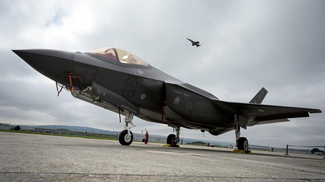 A Lockheed Martin F-35 Lightning II fighter jet is parked on the tarmac at the Payerne Air Base as a Boeing McDonnell Douglas F/A-18 Hornet takes off in the background, during flight and ground tests, as Switzerland is looking for a new fighter jet to replace its aging fleet, on June 7, 2019 in Payerne. Credit: AFP Photo