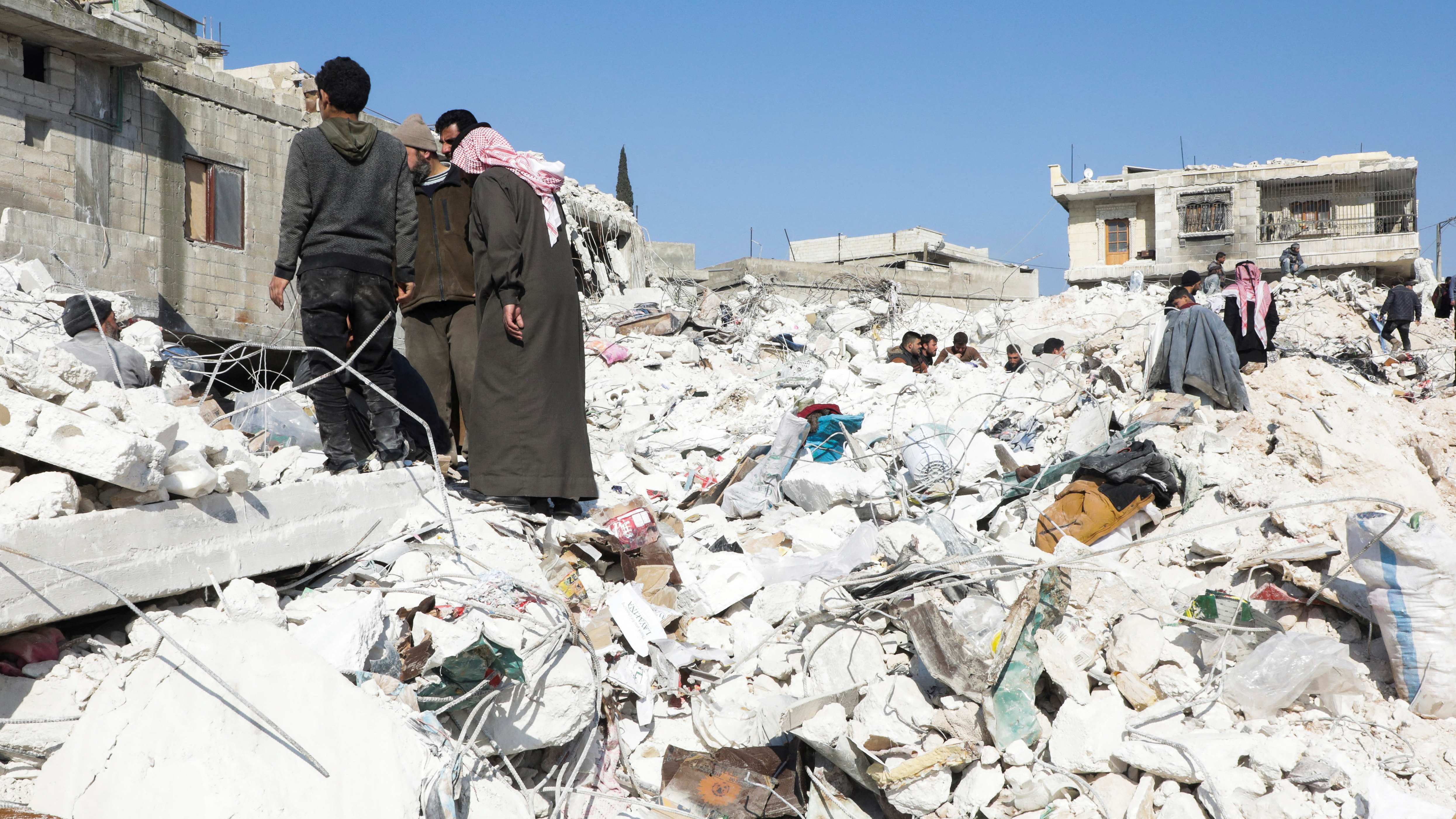 People stand on the rubble of damaged buildings in the aftermath of an earthquake, in rebel-held town of Harem, Syria February 13, 2023. Credit: Reuter Photo