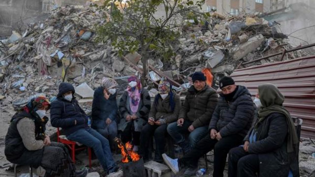 Local residents, whose loved ones are still under the rubble, gather around a bonfire next the collapsed buildings in Hatay, Turkey. Credit: AFP Photo