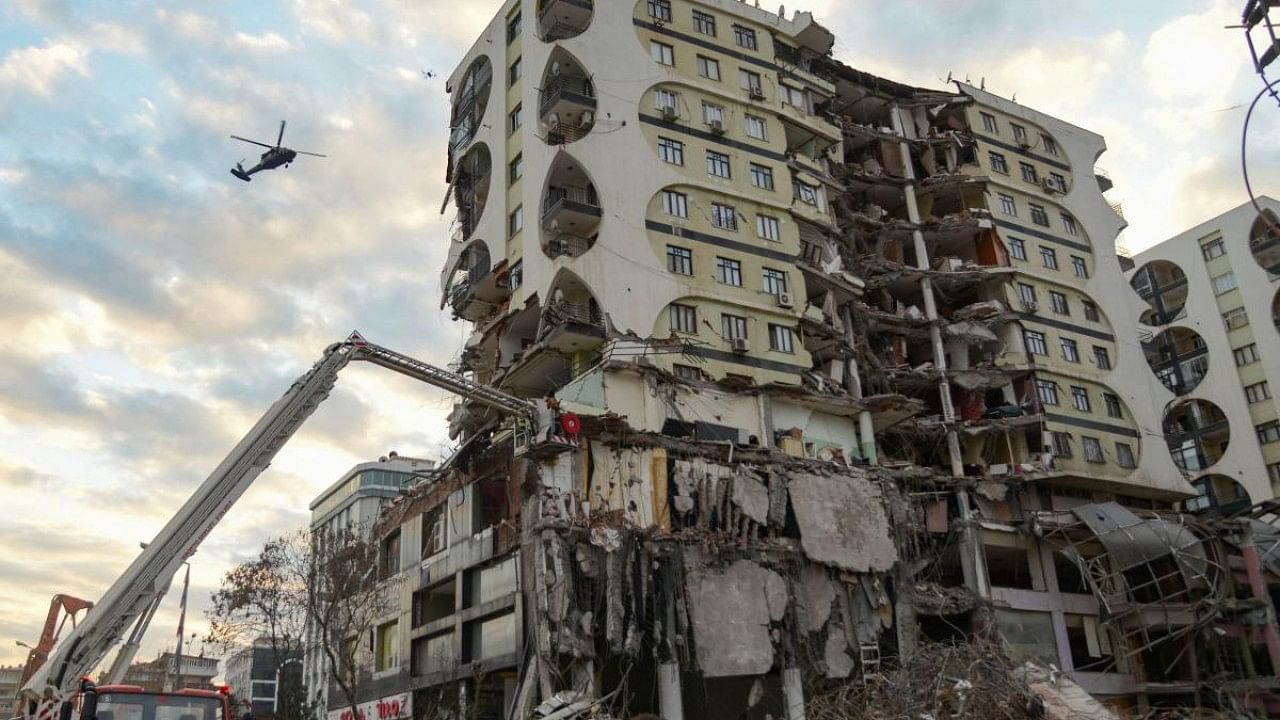 A crane demolishing a damaged building thought to contain several animals and a helicopter flying in the background, in Diyarbakir, south-eastern Turkey. Credit: AFP Photo