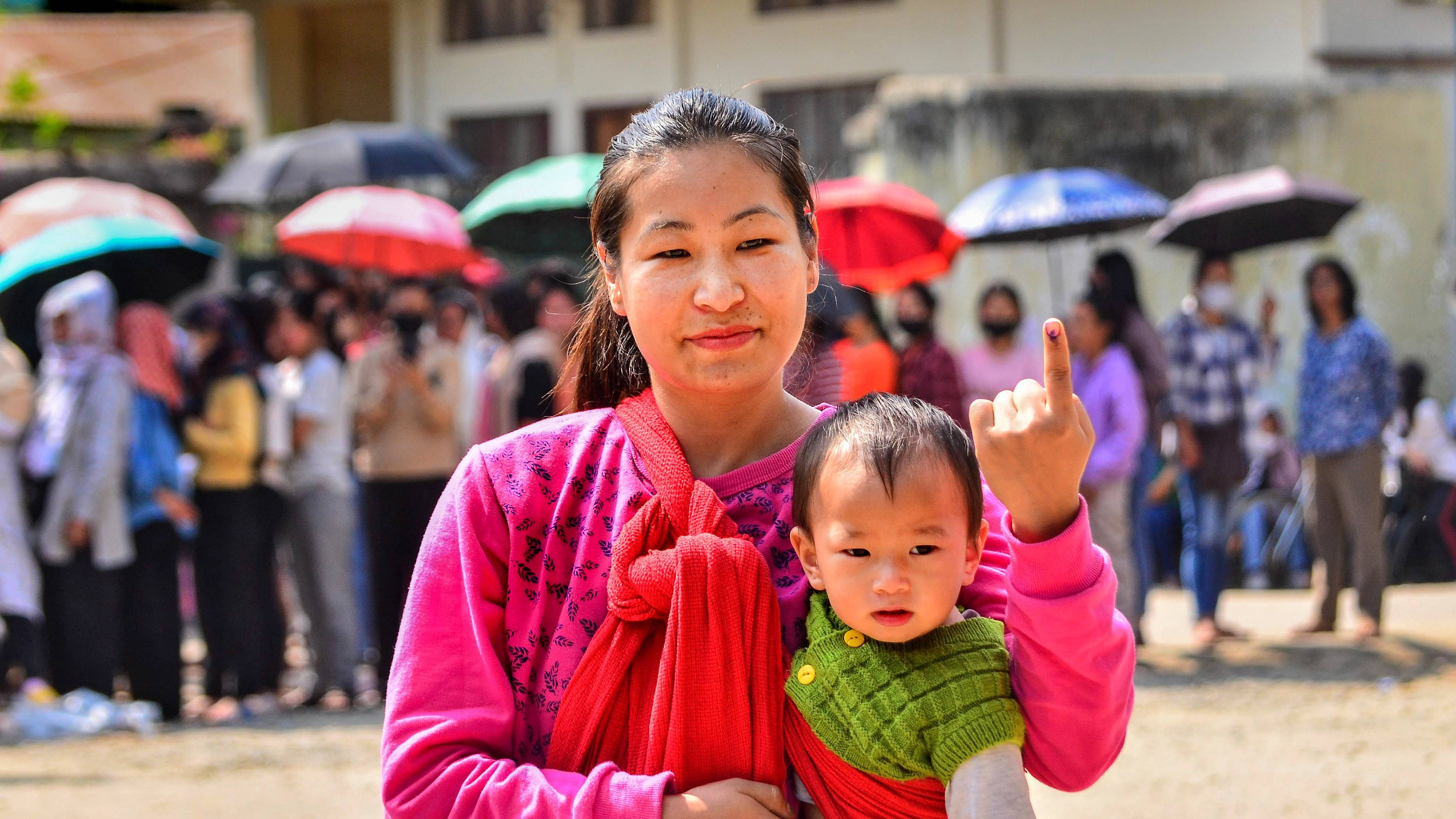 A woman carrying a kid shows her ink-marked finger after casting her vote for the Nagaland Assembly elections. Credit: PTI Photo