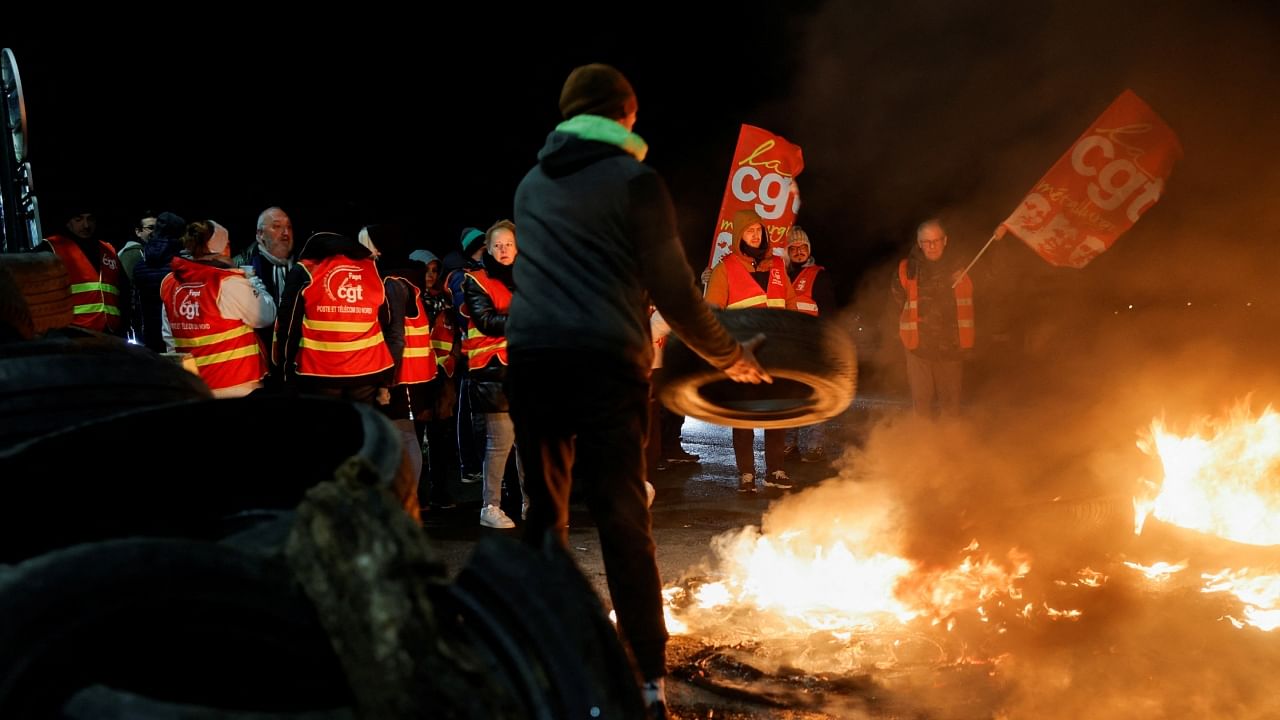 A person throws a tire onto fire as French workers on strike gather and block the entry of a fuel depot as they protest the French government's pension reform plan, in Haulchin, near Valenciennes, France, March 13, 2023. Credit: Reuters Photo