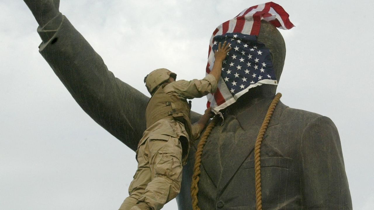  In this file photo dated April 9, 2003 a US Marine covers the face of Iraqi President Saddam Hussein's statue with the US flag in Baghdad's al-Fardous square. - Twenty years after the US-led invasion of Iraq toppled Saddam Hussein, the oil-rich country remains deeply scarred by the conflict and, while closer to the United States, far from the liberal democracy Washington had envisioned. Credit; AFP Photo