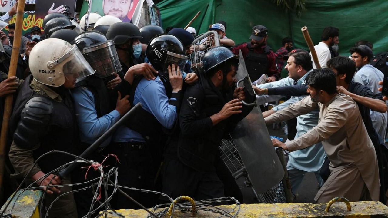 Supporters (R) of former prime minister Imran Khan try to stop riot police scuffle outside Khan's house to prevent officers from arresting him. Credit: AFP Photo