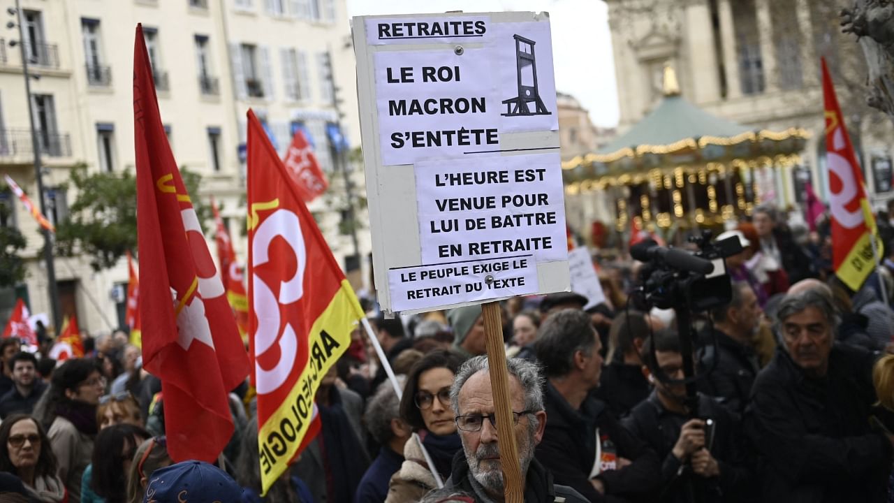 Protesters march holding a placard which reads as "Pensions. Macron the King is stubborn. Time for him to retreat from the scene. The people demand the removal of the law", during a demonstration in Marseille, southern France, on March 18, 2023, two days after the French government pushed a pensions reform through parliament without a vote, using the article 49.3 of the constitution. Credit: AFP Photo