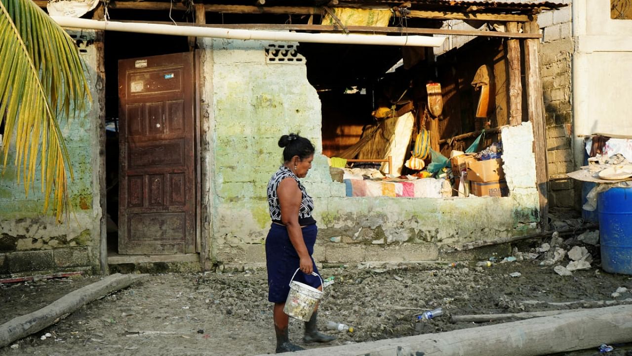 A woman passes by a damaged house following an earthquake in Isla Puna, Ecuador. Credit: Reuters Photo