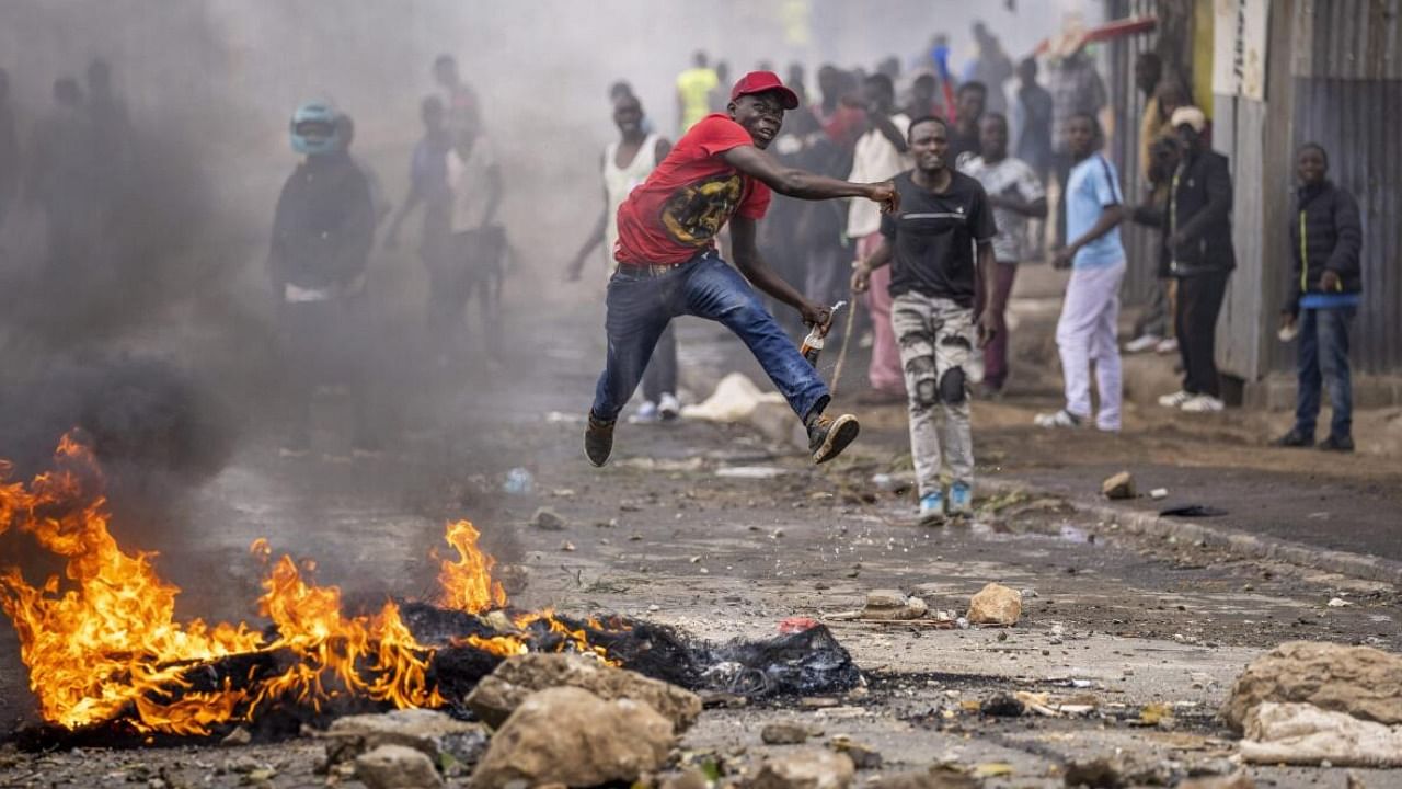 A protester jumps in the air as he throws a rock towards police next to a burning barricade in the Kibera slum of Nairobi. Credit: AP/PTI Photo 
