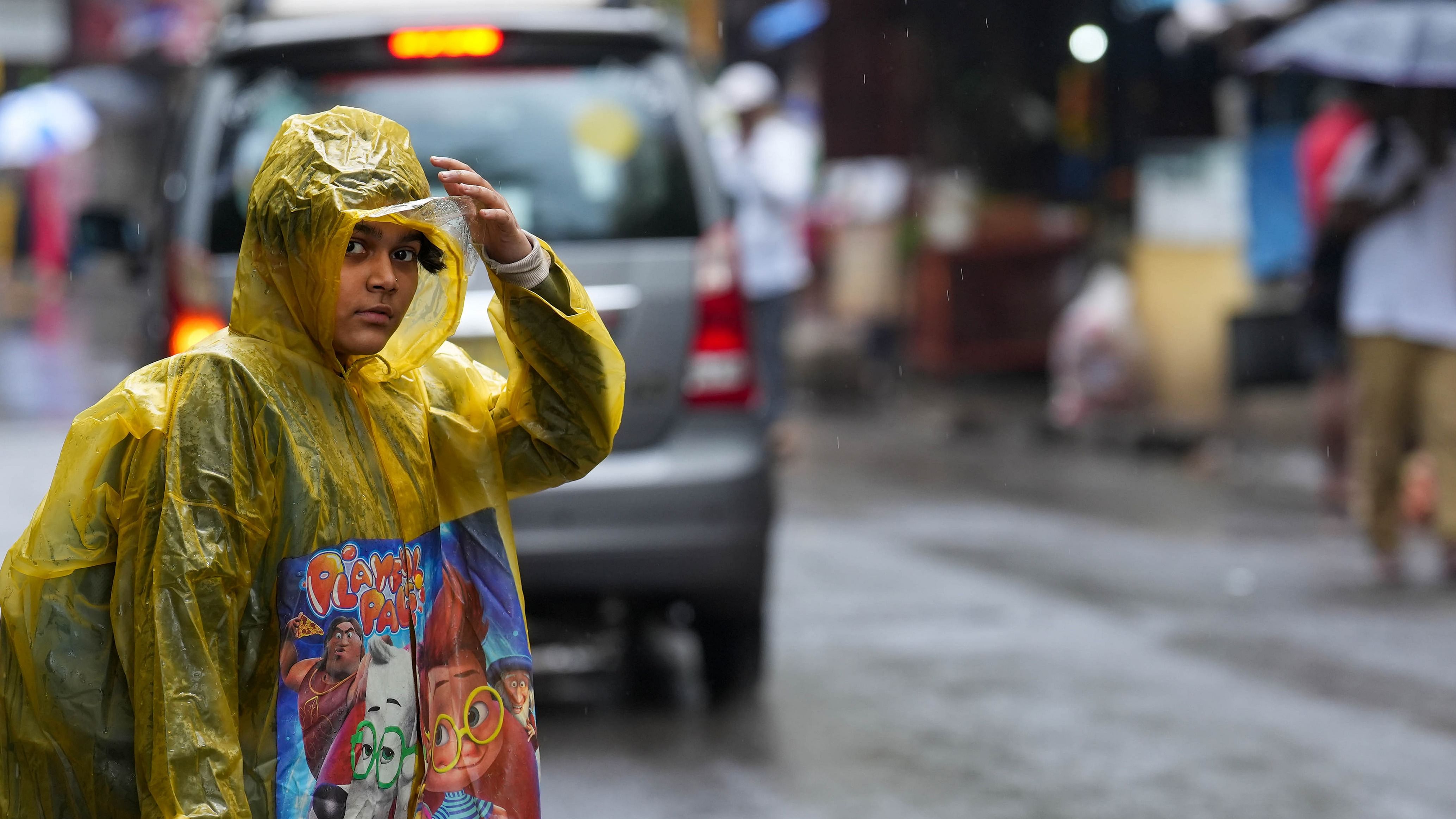  A girl wearing a raincoat attempts to cross a road amid rains, in Mumbai, Tuesday, March 21, 2023. Credit: PTI Photo