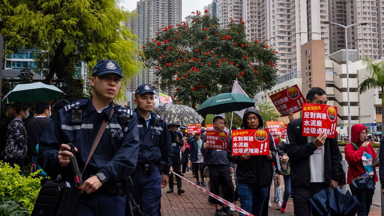 Police watch protesters walking within a cordon line wearing number tags during a rally in Hong Kong, Sunday, March 26, 2023. Dozens of people on Sunday joined Hong Kong's first authorized demonstration against the government since the lifting of major Covid-19 restrictions under unprecedentedly strict rules, including wearing a numbered badge around their necks. The banners read 'Oppose the building of cement plant and rubbish processing facility'. Credit: AP/PTI Photo