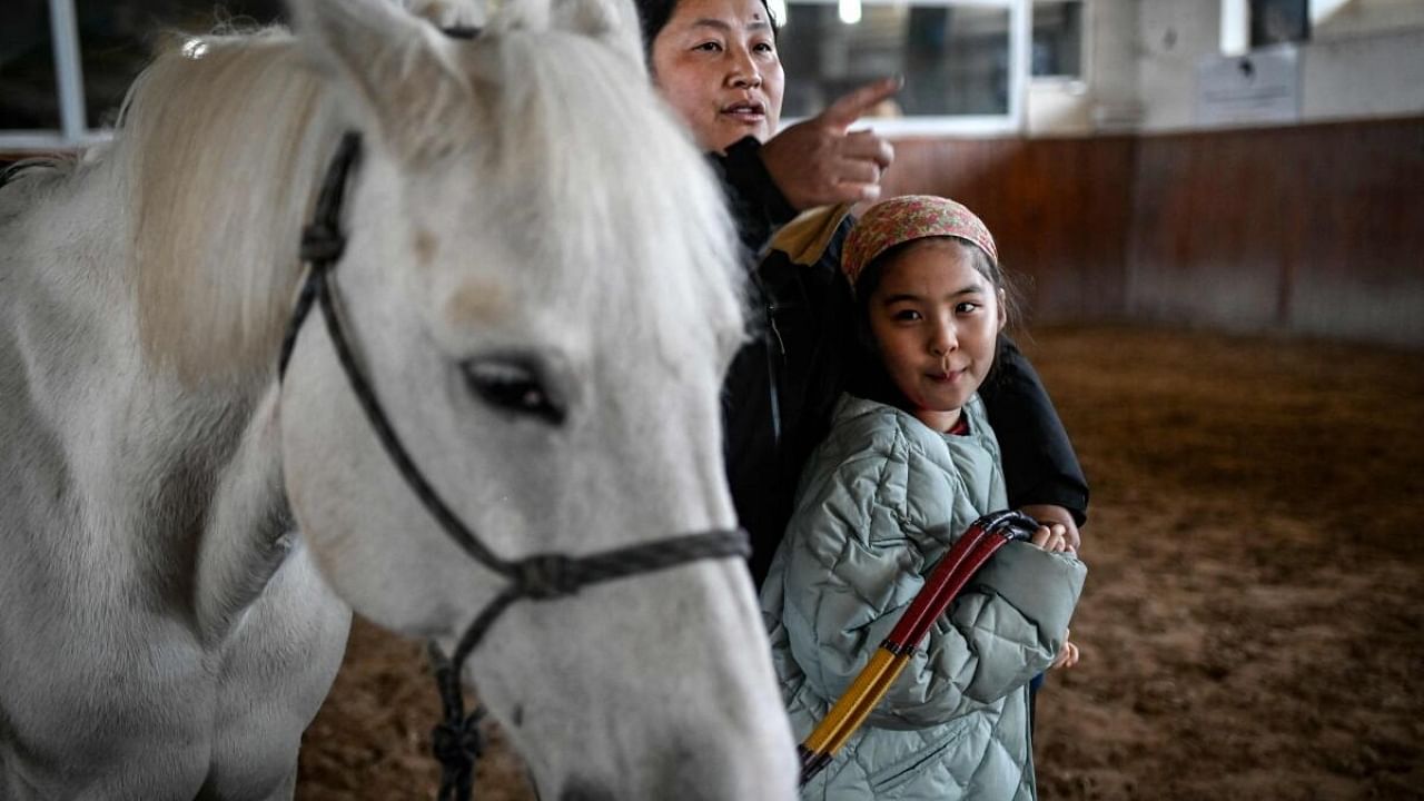 A young girl with autism spectrum disorder looking at her horse before a riding lesson at a horse club in Beijing. Credit: AFP Photo