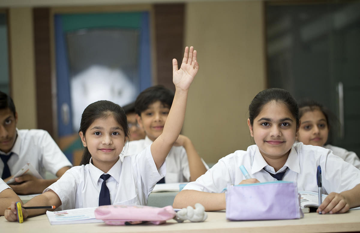 A smiling girl raising her hand to answer a question in the classroom