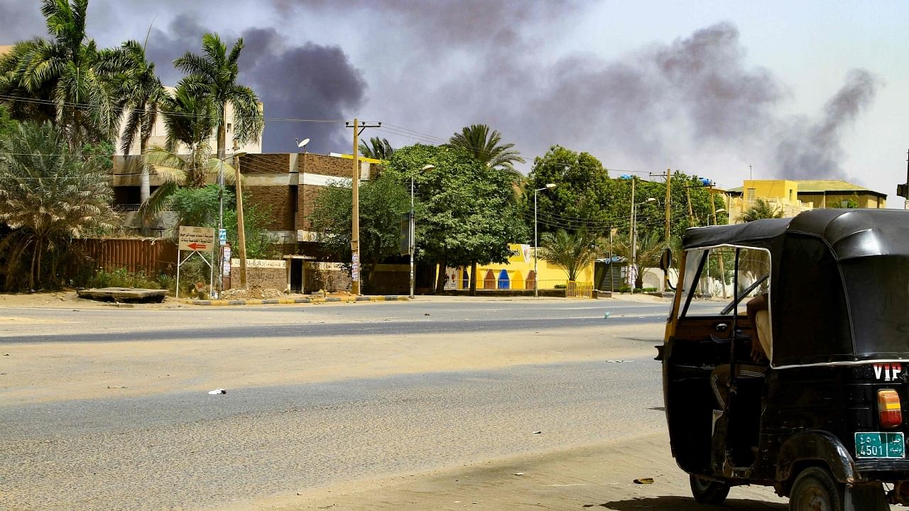 Smoke rises from buildings as a taxi driver sits in his vehicle along a deserted street in Khartoum. Credit: AFP Photo