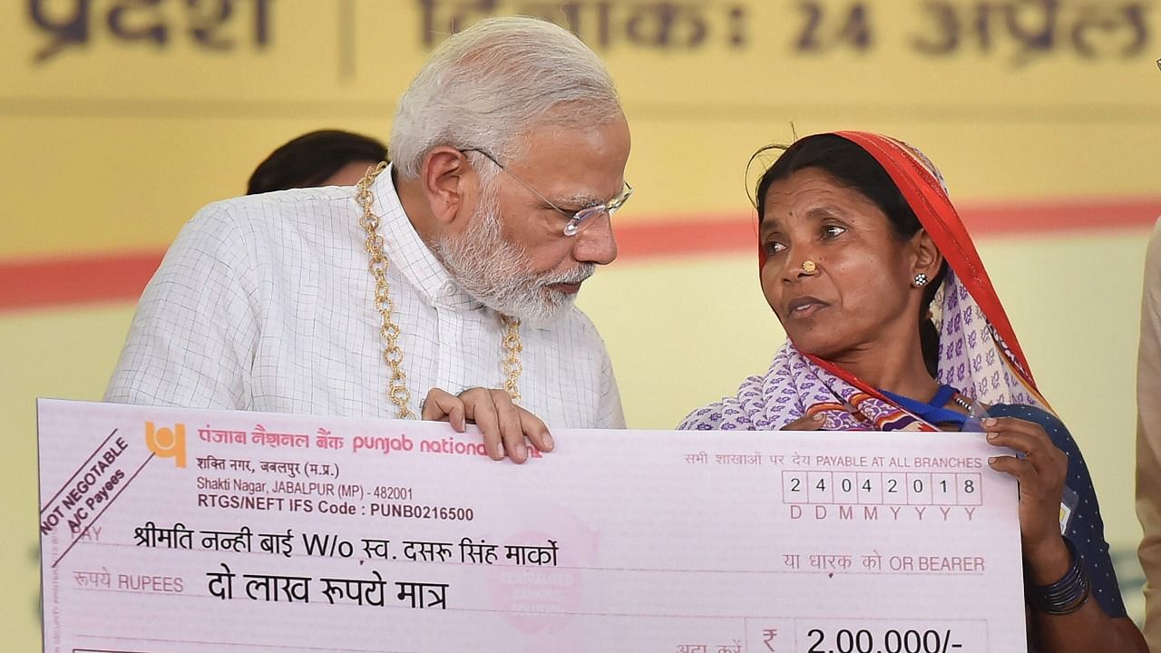 Prime Minister Narendra Modi hands over the cheque of Rs 2 lakh to Nanhi Bai Marko, under Pradhan Mantri Jeevan Jyoti Beema Yojana. Credit: PTI File Photo