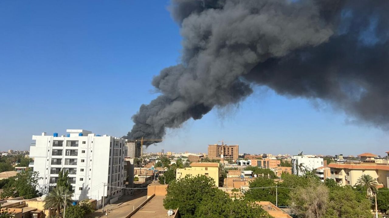 A column of smoke rises behind buildings near the airport area in Khartoum. Credit: AFP Photo