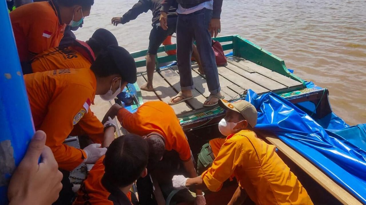This handout picture taken and released on April 28, 2023 by the Indonesia Search and Rescue Agency (BASARNAS) shows rescue workers moving victim's bodies after a passenger boat overturned shortly after leaving Tembilahan port in Indragiri Hilir Regency a day earlier. - Eleven people drowned in western Indonesia after a passenger boat carrying dozens overturned, an official said on April 28. Credit: AFP Photo