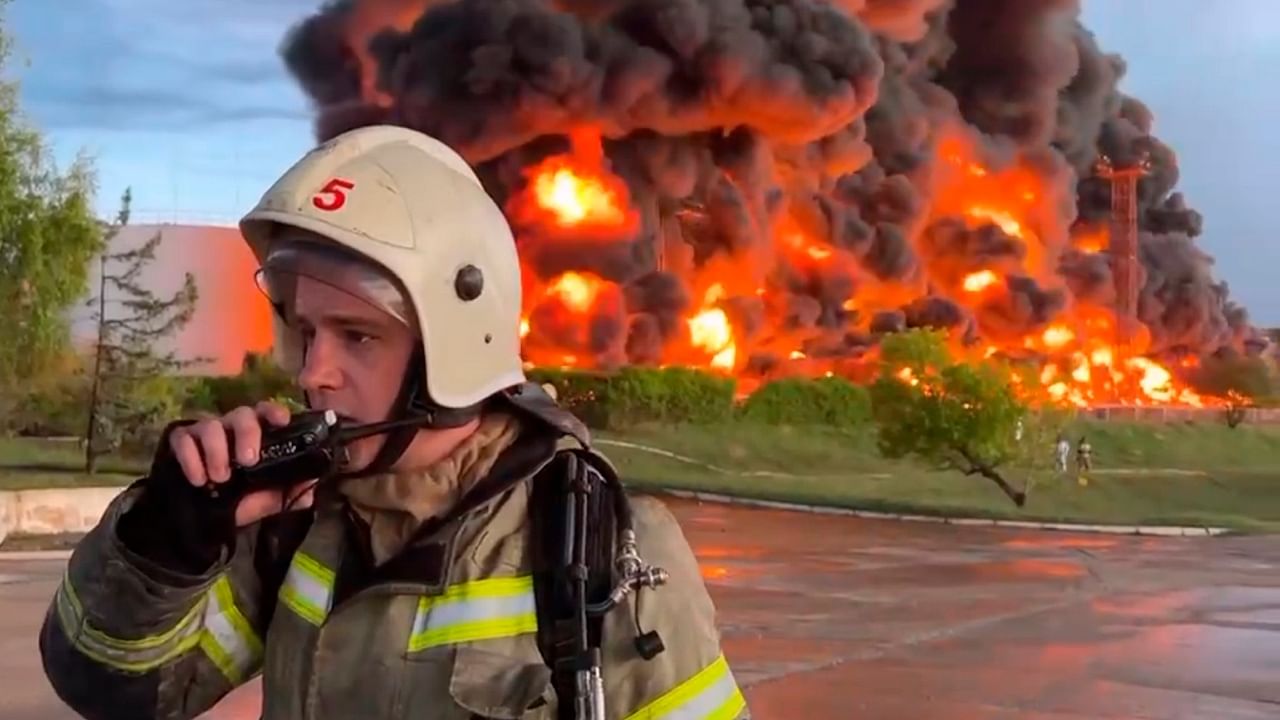 A firefighter speaks on the walkie talkie as smoke and flame rise from a burning fuel tank in Sevastopol, Crimea. A massive fire erupted at an oil reservoir there after it was hit by a drone. Credit: AP/PTI Photo