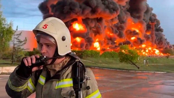 A firefighter speaks on the walkie talkie as smoke and flame rise from a burning fuel tank in Sevastopol, Crimea. A massive fire erupted at an oil reservoir there after it was hit by a drone. Credit: AP/PTI Photo  