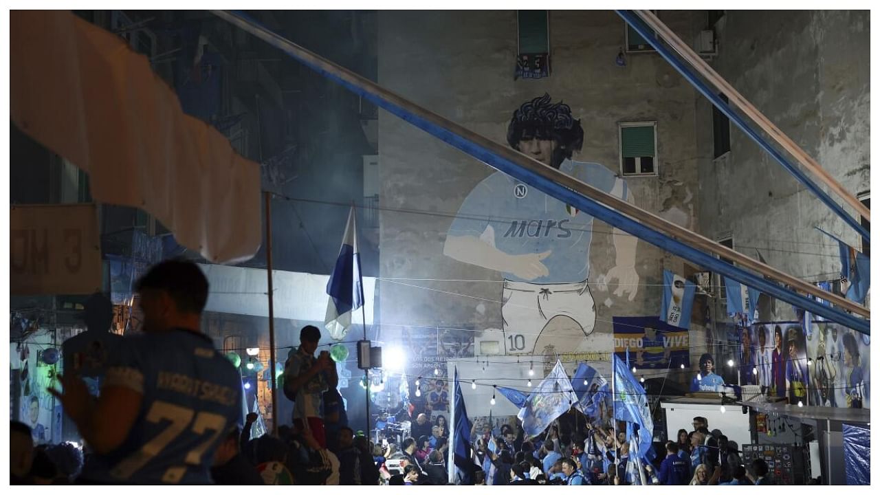 With a mural of Diego Maradona in the background, Napoli fans celebrate after winning the Serie A soccer match between Udinese and Napoli in Naples, Italy, Thursday May 4, 2023. Credit: AP/PTI Photo