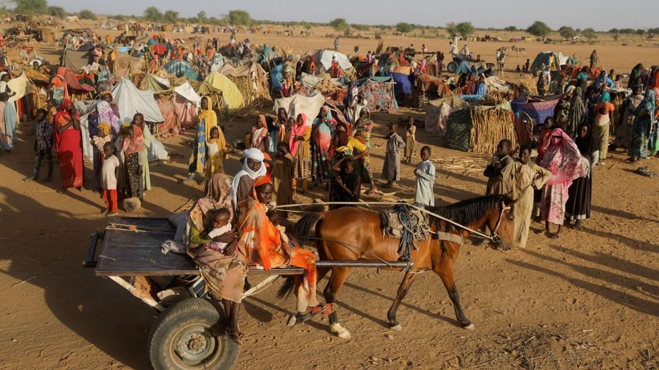 Sudanese refugees who fled the violence in their country, ride a cart as they pass other refugees standing beside makeshift shelters near the border between Sudan and Chad in Koufroun, Chad May 6, 2023. Credit: Reuters Photo