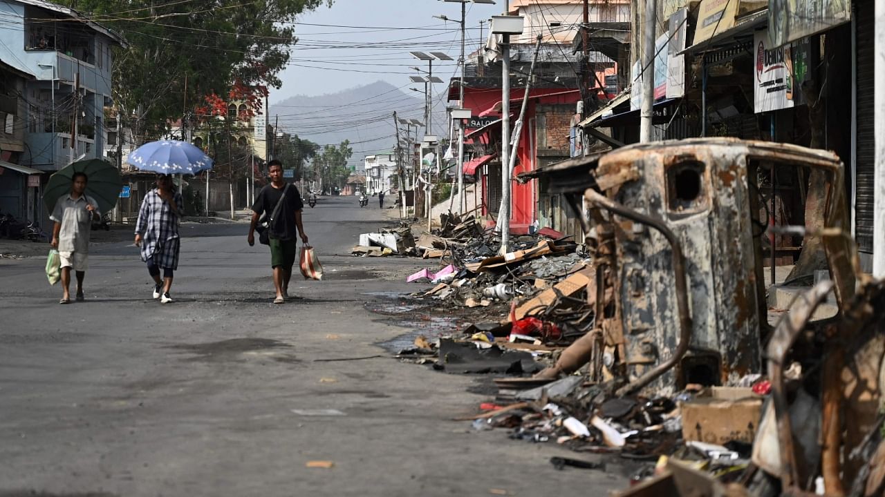 People walk past a burnt vehicle and rubble on a street in Churachandpur in violence-hit areas of northeastern Indian state of Manipur. Credit: AFP Photo