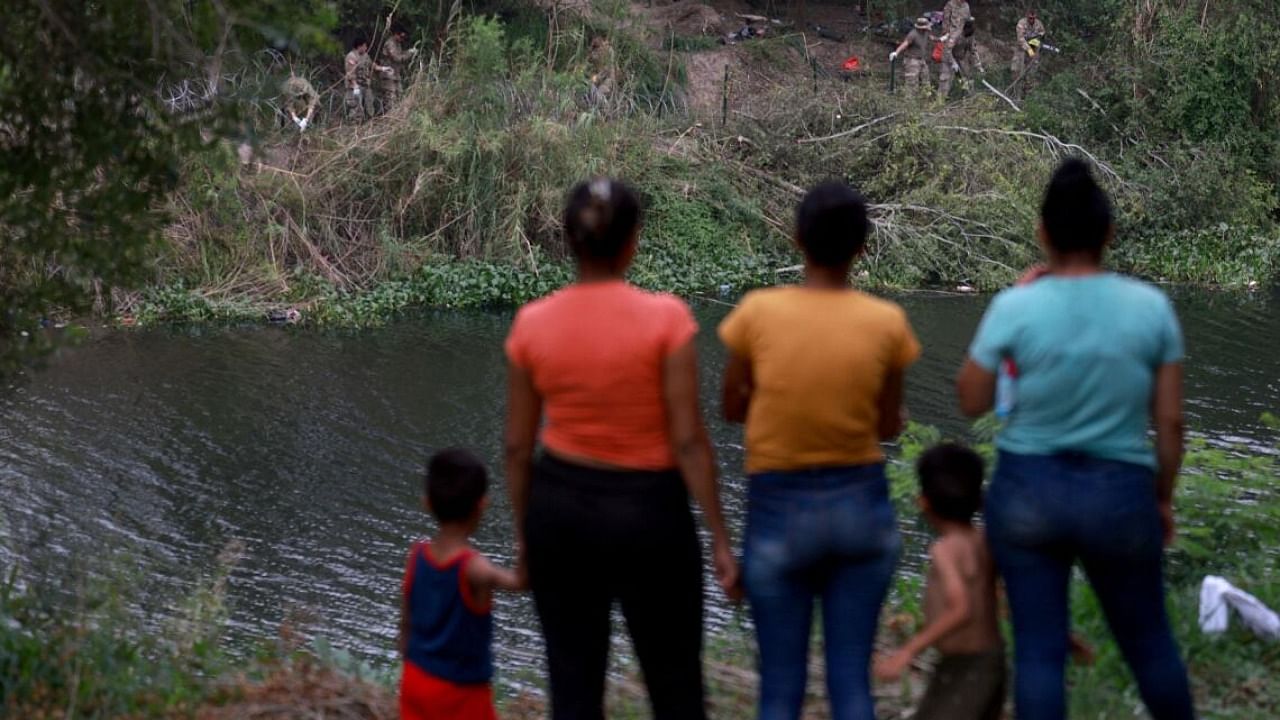 Migrants watch as Texas National Guardsmen clear an area of the U.S. side of the Rio Grande. Credit: AFP